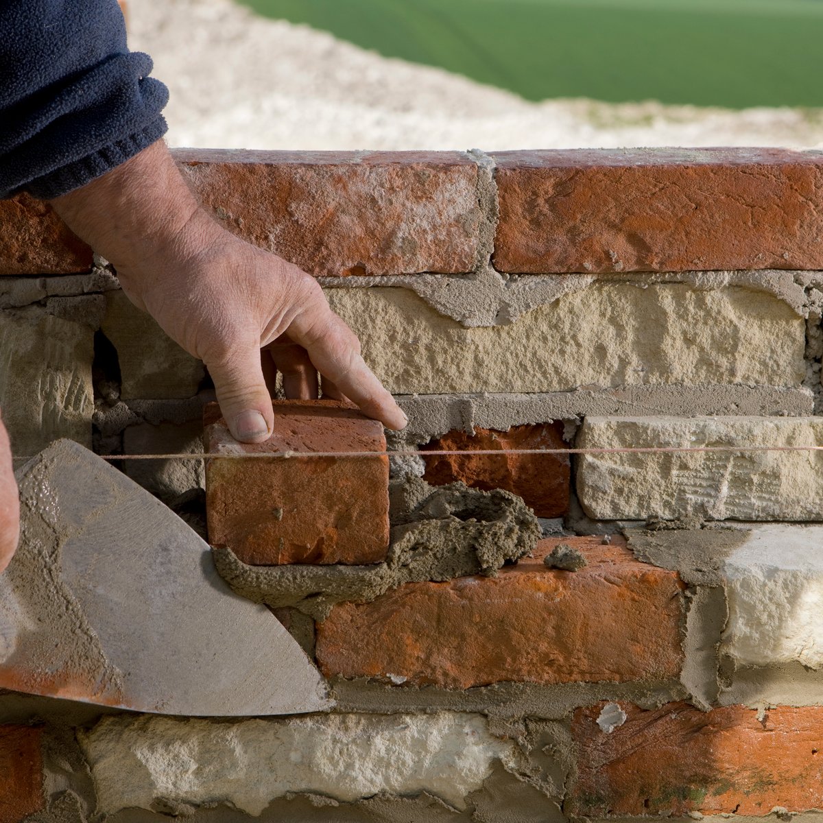 Mason's hand setting a replacement red brick into a wall with a trowel and mason's line - brick repair and replacement service in Chicago, IL by MasonryPros.us
