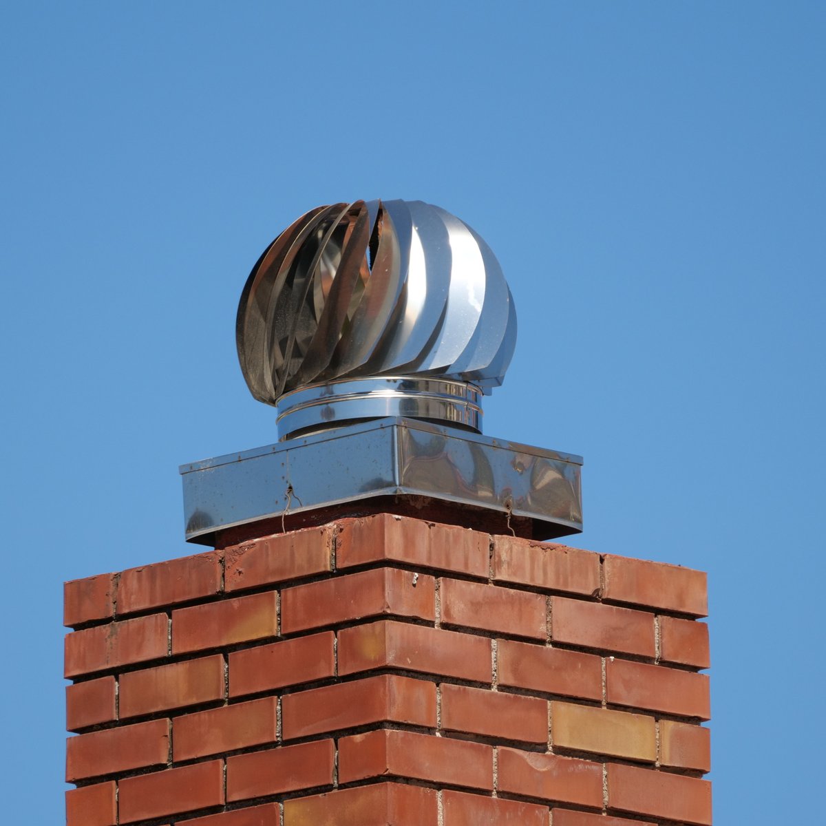 Red brick residential chimney topped with a stainless spinning turbine cap against a blue sky - chimney repair in Chicago, IL by MasonryPros.us