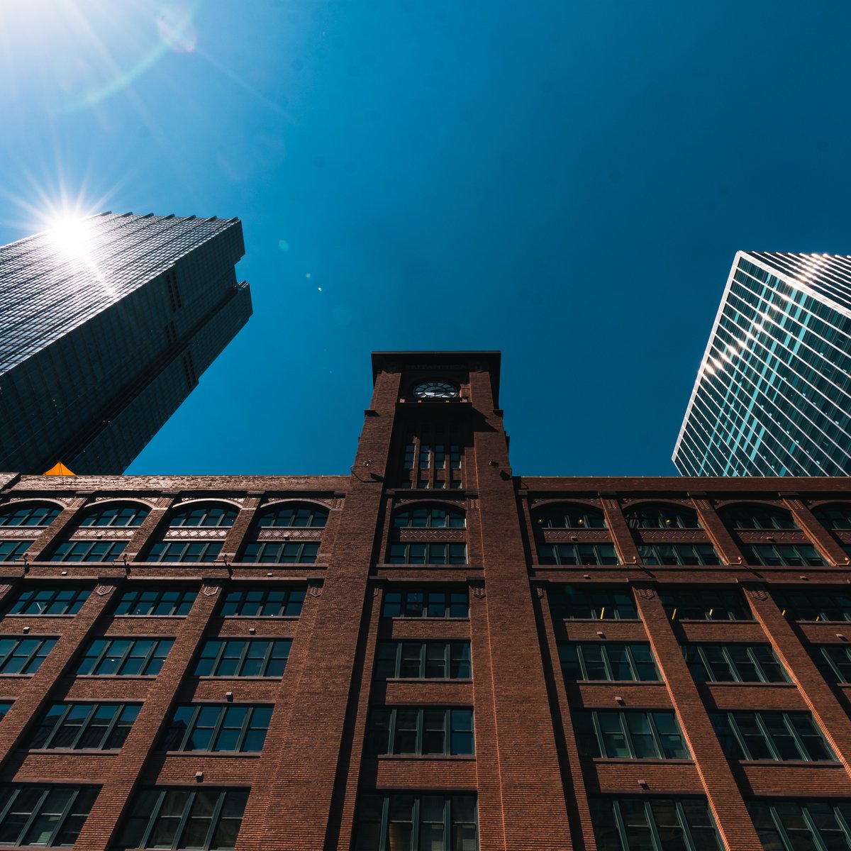 Upward view of a historic Chicago brick commercial building with a clock tower framed by glass towers - historic and landmark masonry restoration in Chicago, IL by MasonryPros.us