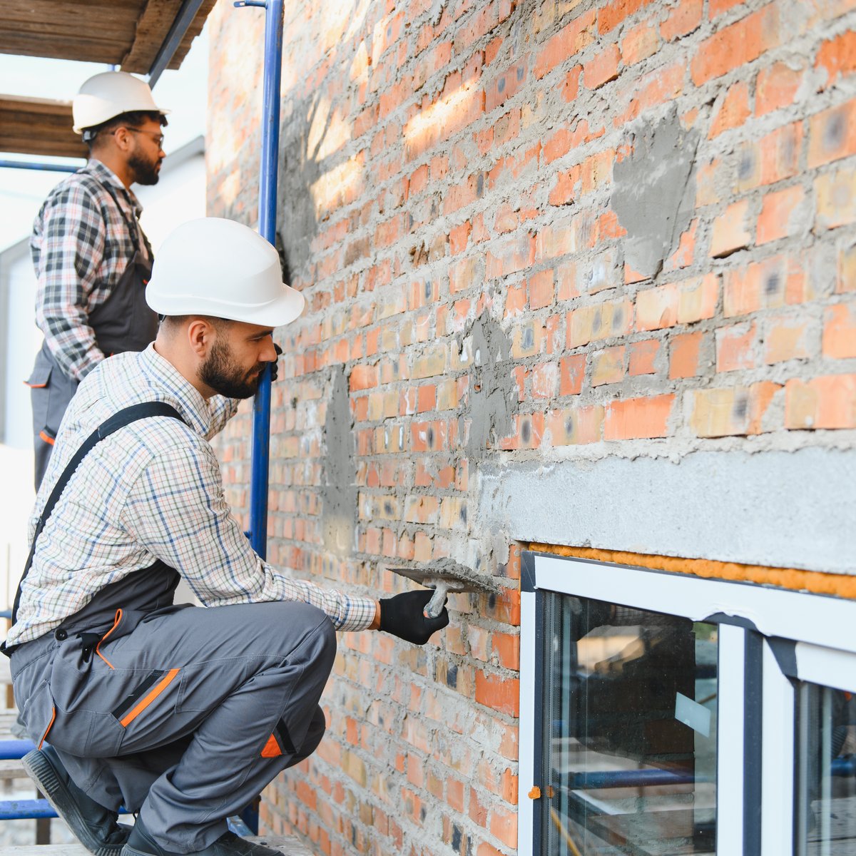 Two hard-hatted masons on scaffolding repairing brickwork above a window opening - steel lintel replacement in Chicago, IL by MasonryPros.us