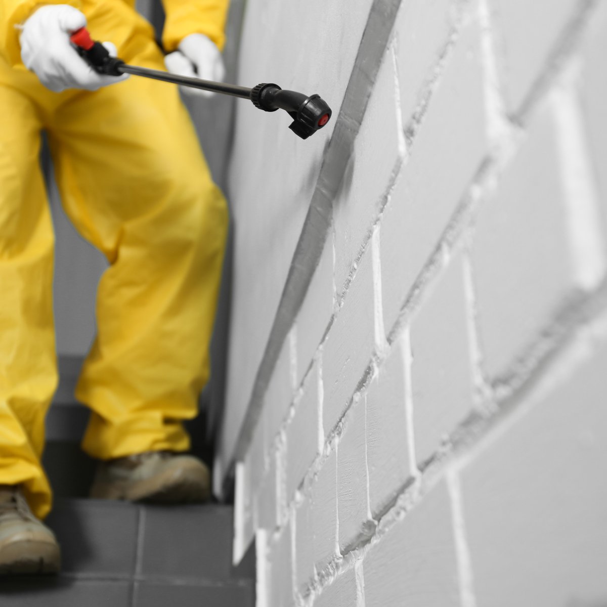 Worker in a yellow protective suit rolling a waterproof coating onto a grey brick wall - masonry waterproofing and sealing in Chicago, IL by MasonryPros.us