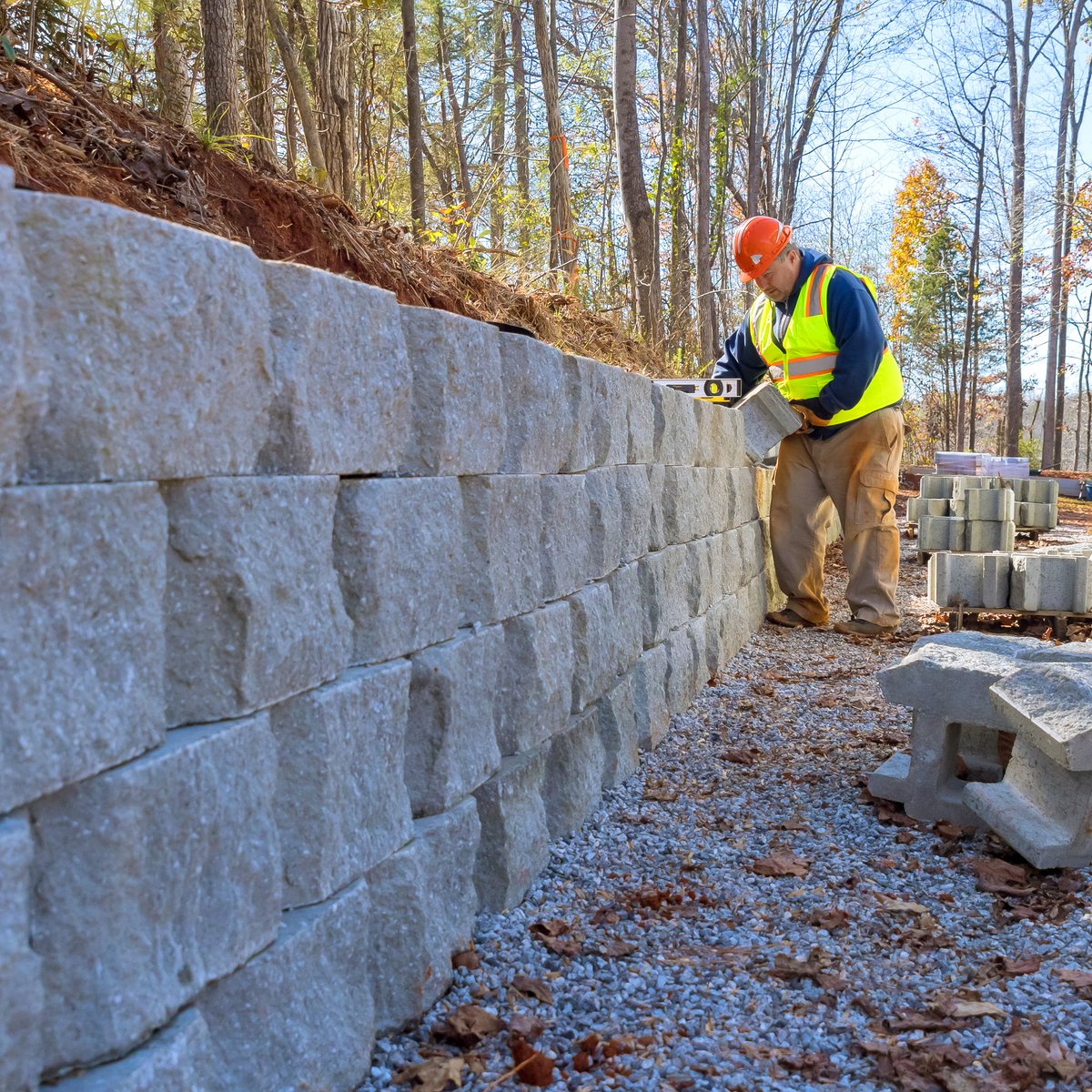 Worker leveling a course on a segmental grey block retaining wall on a wooded slope - retaining wall construction and repair in Chicago, IL by MasonryPros.us