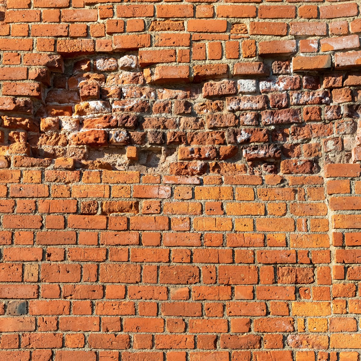 Aged orange brick wall with a large patch of spalled, crumbling, water-damaged brick faces - spalling brick repair in Chicago, IL by MasonryPros.us